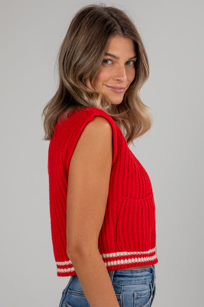 Woman wearing a red sleeveless knitted top against a gray background