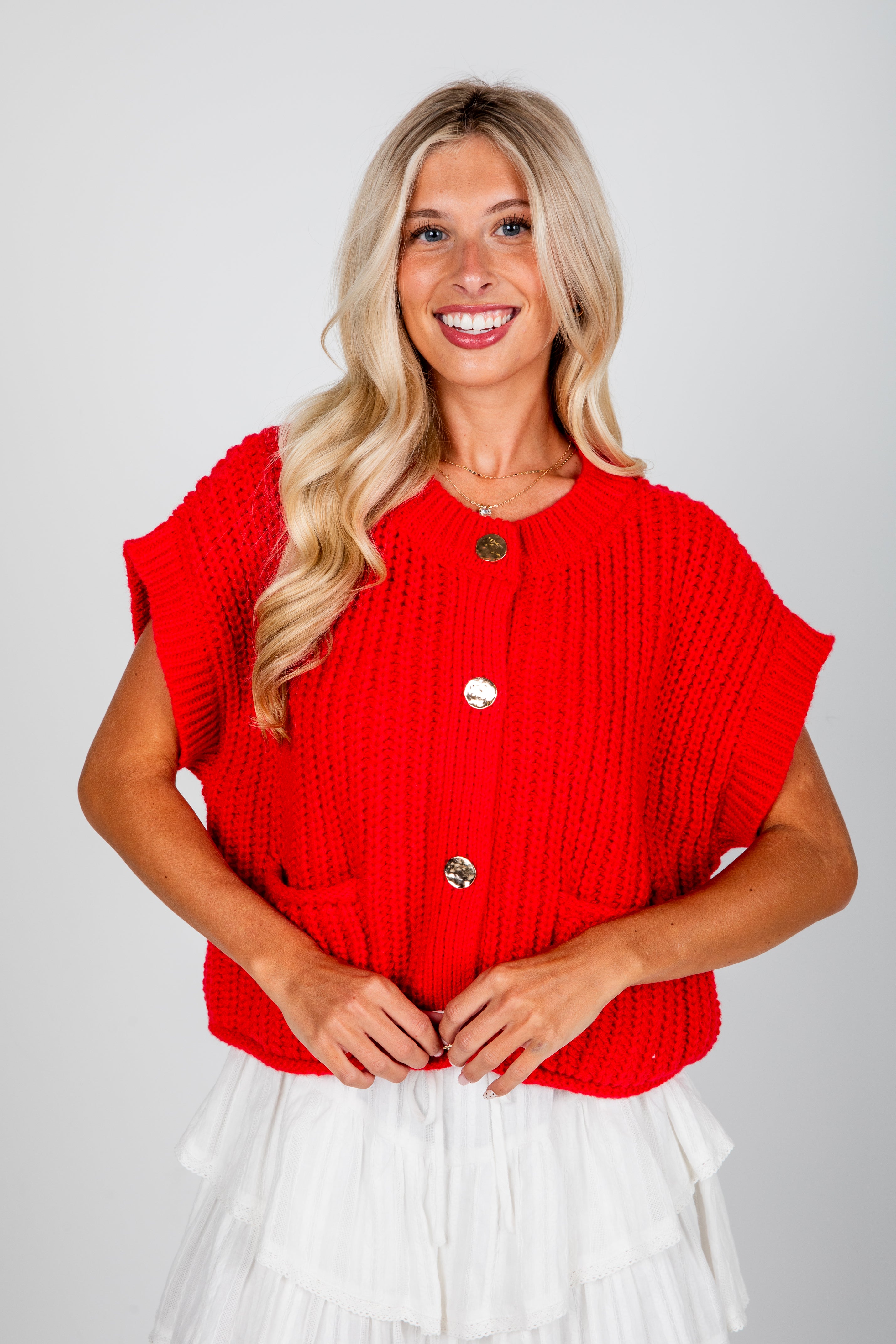 Woman wearing a red sleeveless top with buttons on a plain background