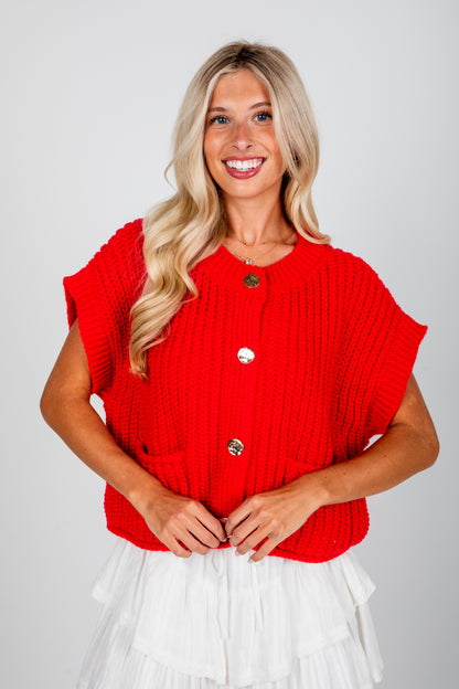 Woman wearing a red sleeveless top with buttons on a plain background