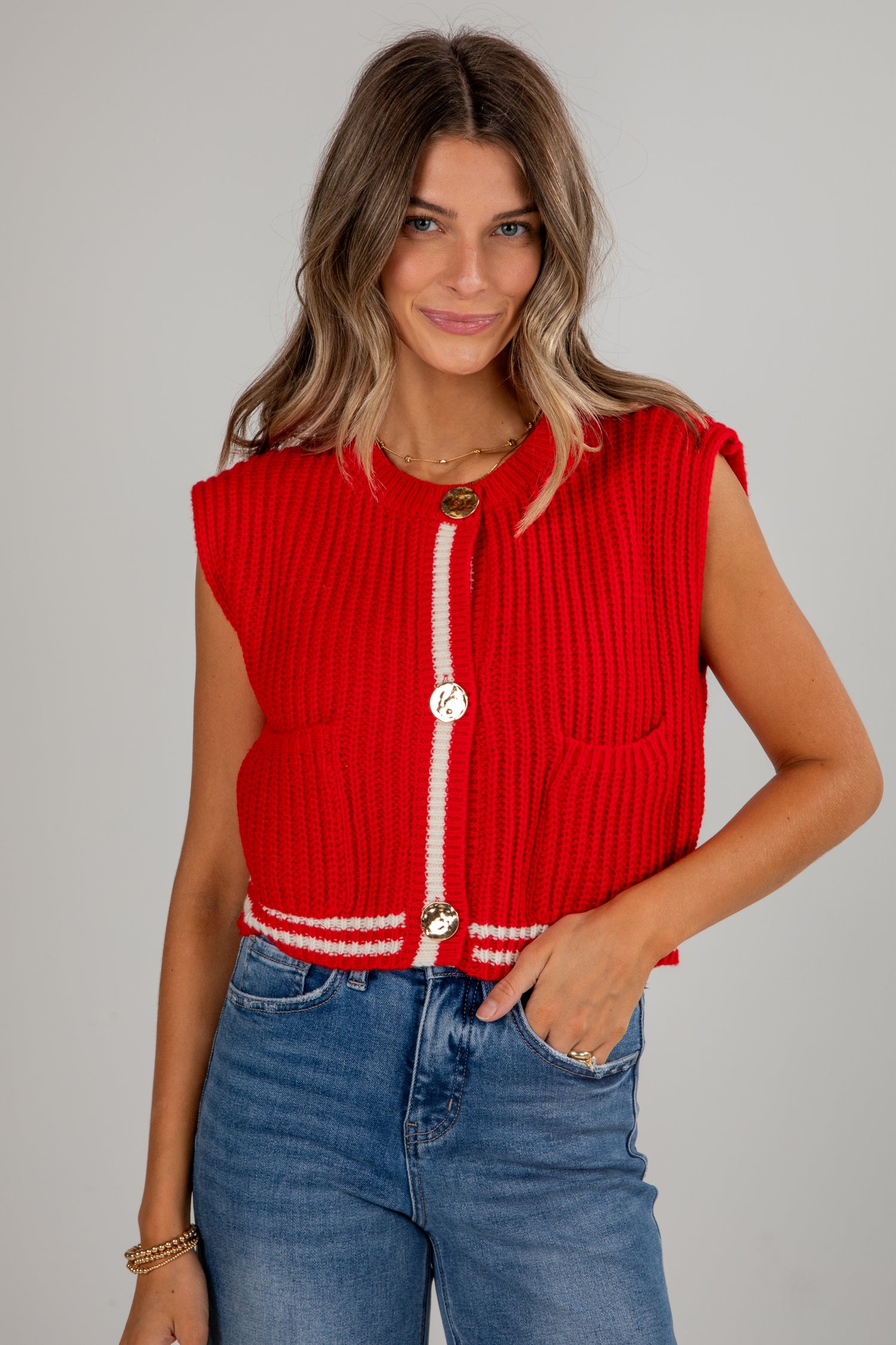 Woman wearing a red sleeveless vest with white trim against a gray background