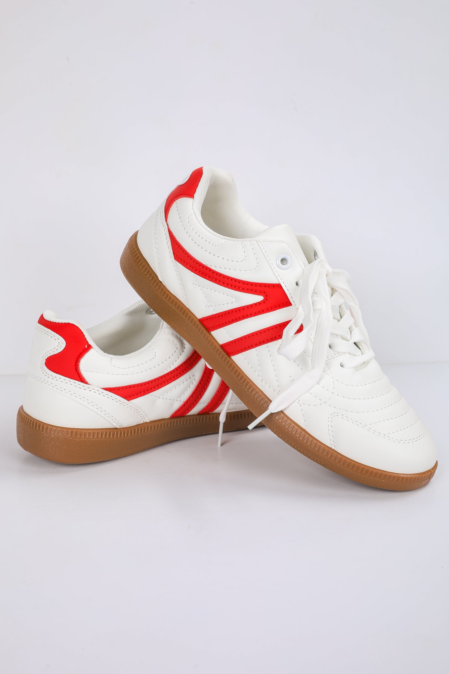 White sneakers with red accents and brown soles on a light gray background