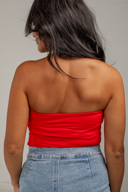 A woman shown from behind wearing a bright red strapless bandeau top and light blue denim jeans against a plain light gray wall.