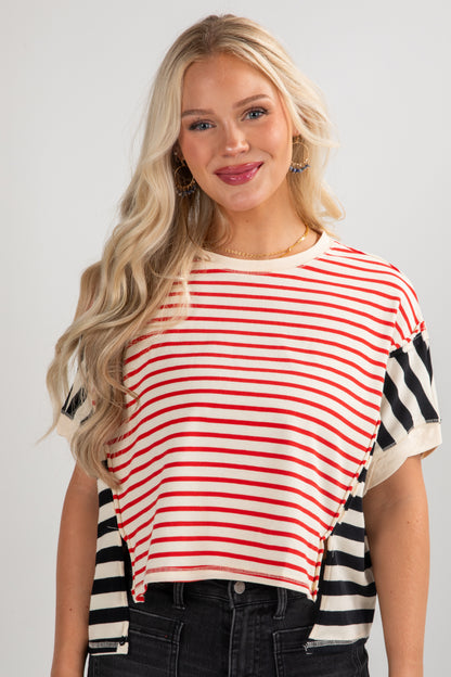 Woman wearing a red and white striped top with black and white striped sleeves on a plain background