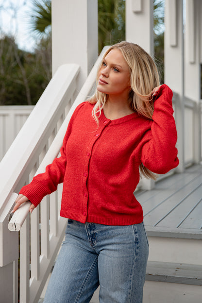 Woman wearing a red sweater and blue jeans standing on a wooden deck.