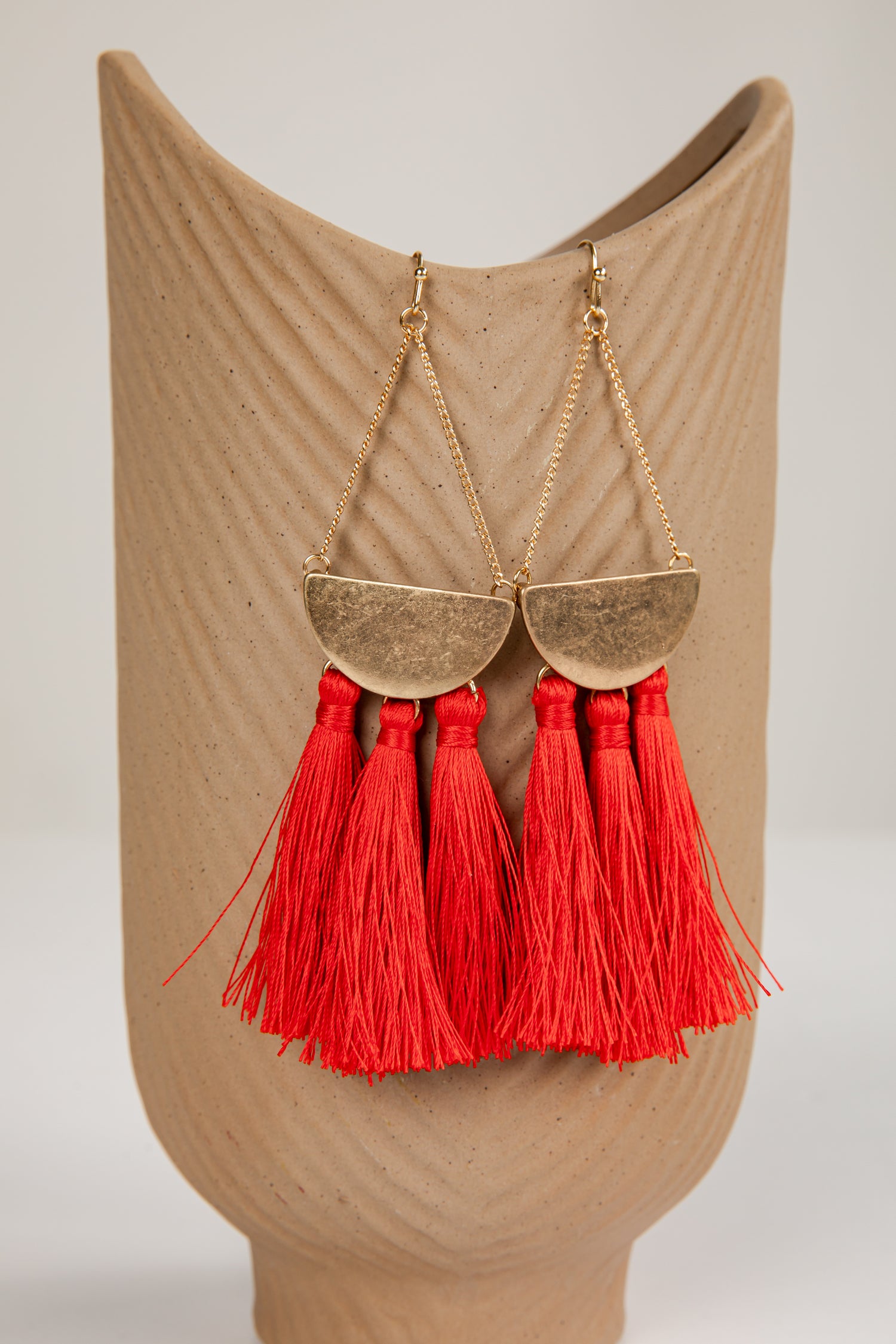 Gold earrings with red tassels on a beige mannequin bust.