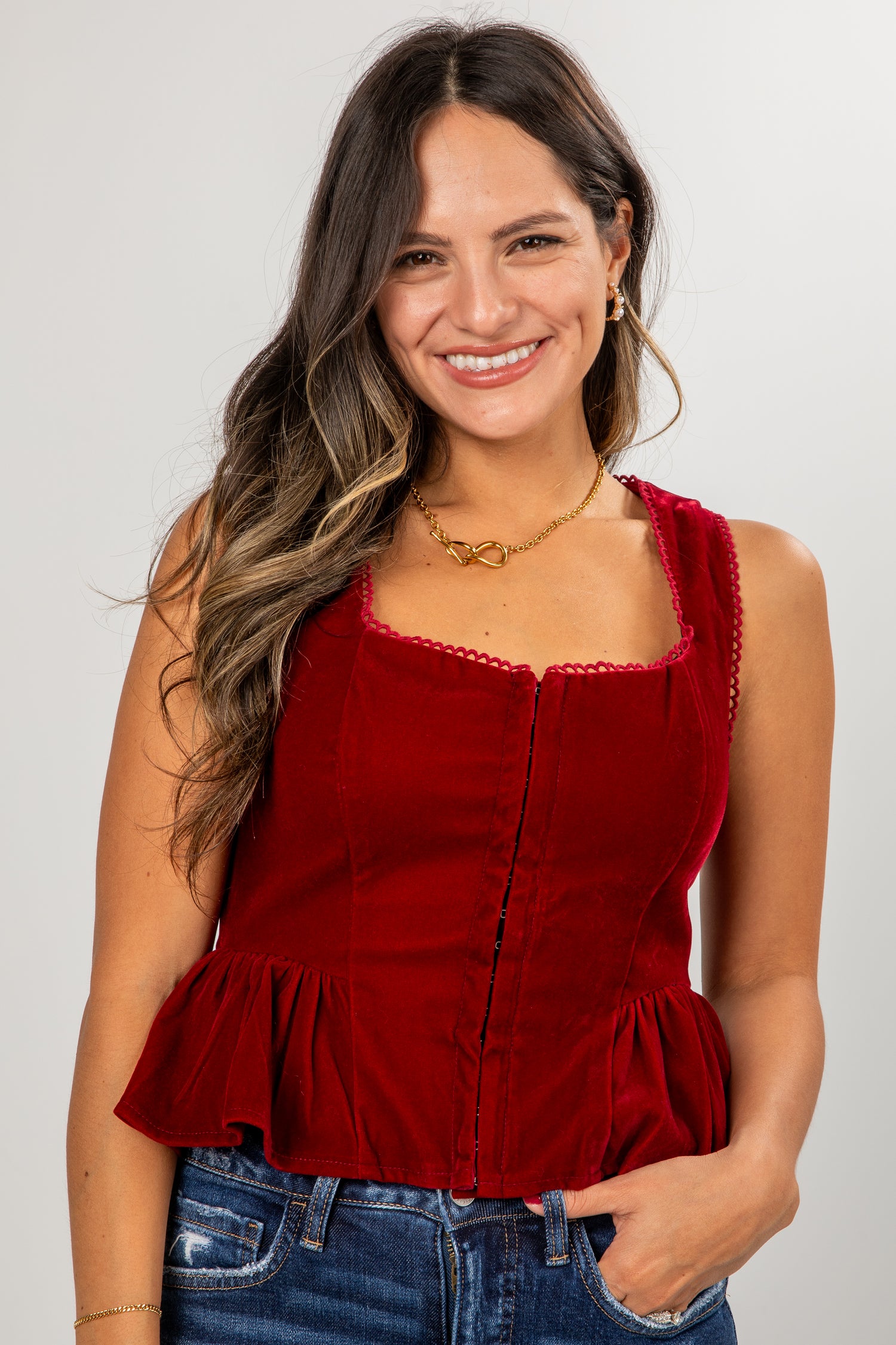 Woman wearing a red peplum top and blue jeans against a plain background