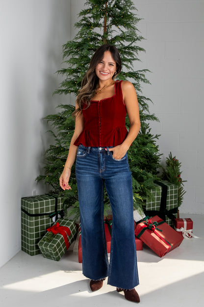 Woman in a red top and blue jeans standing in front of a Christmas tree with presents.