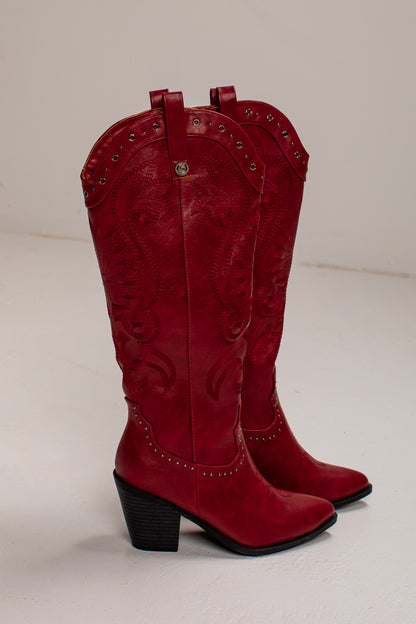 A pair of red leather cowboy boots with embossed western stitching, silver-tone studs, and black block heels, photographed against a plain off-white background.