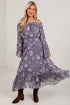 A woman modeling an off-the-shoulder midi dress in a dusty purple floral print, paired with brown suede ankle boots, standing against a plain white studio wall.