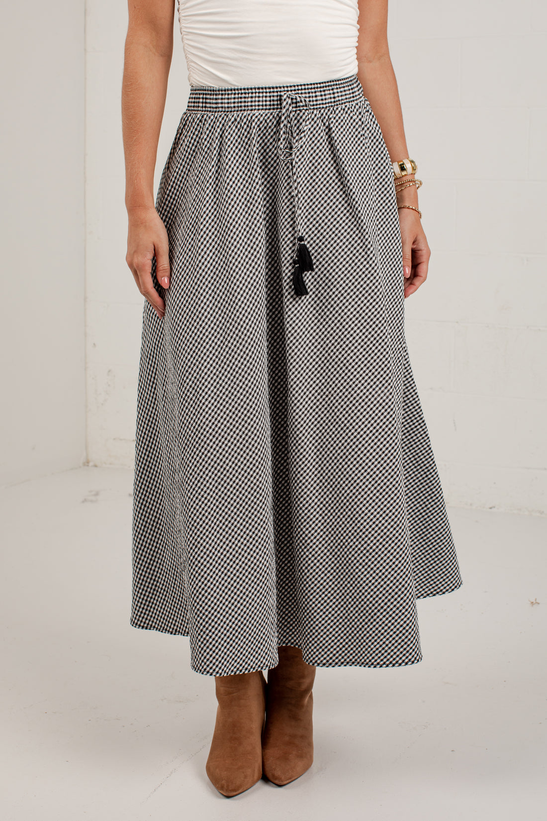 A woman wearing a black and white micro-checkered midi skirt with a drawstring waist, paired with a white top and brown suede ankle boots.