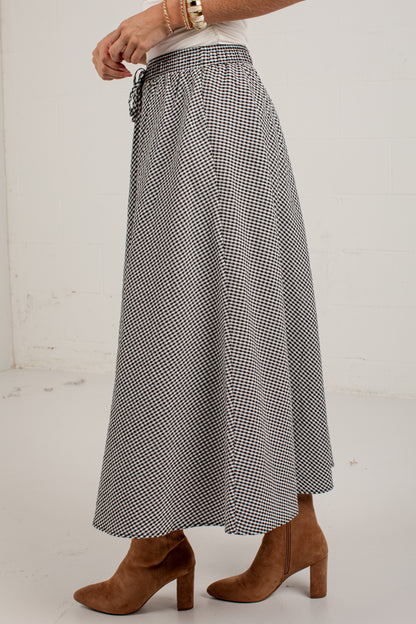 A person wearing a black and white gingham patterned maxi skirt with a drawstring waist, styled with a white top and brown suede block-heel ankle boots.