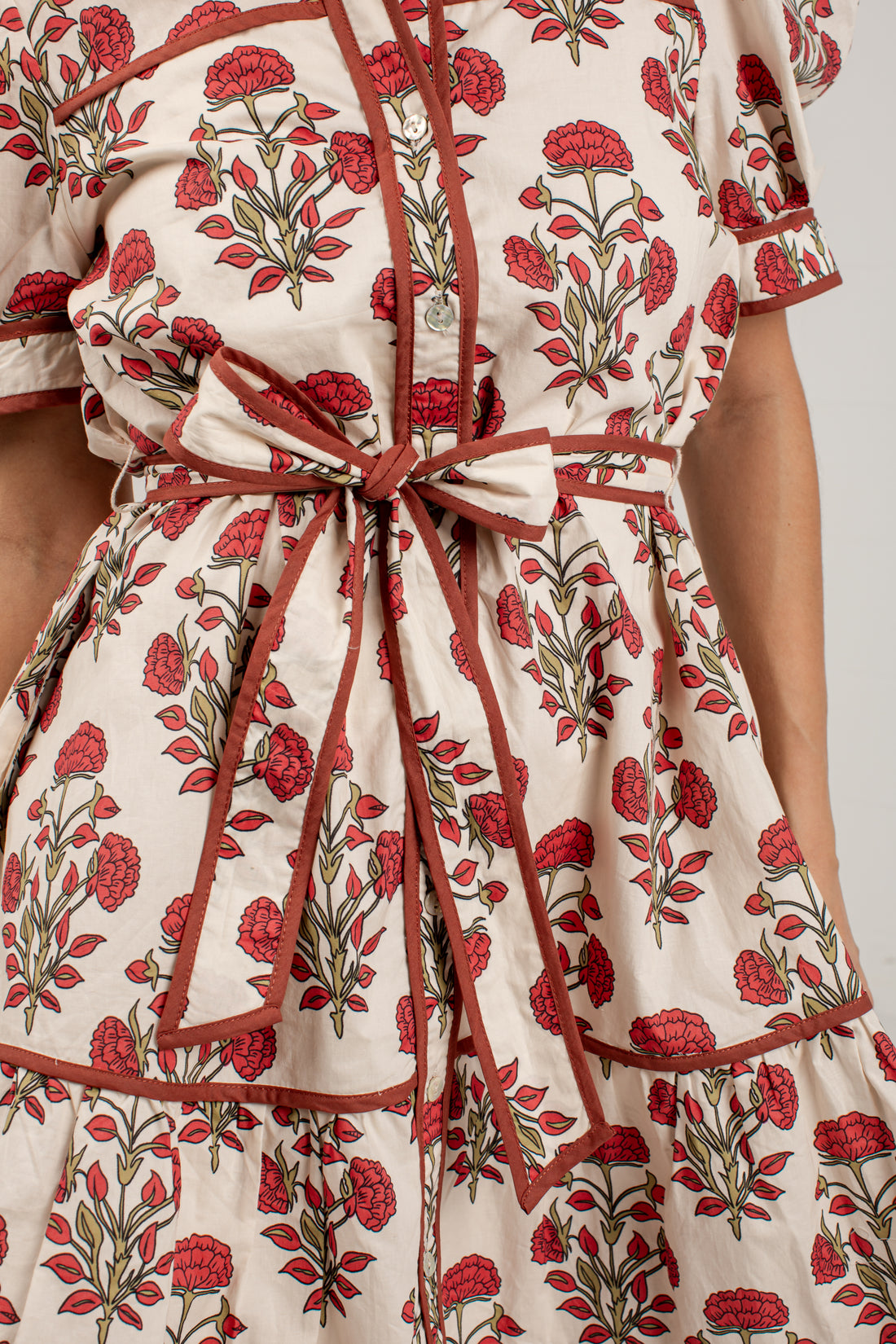 Close-up of a cream-colored dress with a red and green floral block print, featuring a matching fabric tie belt at the waist.