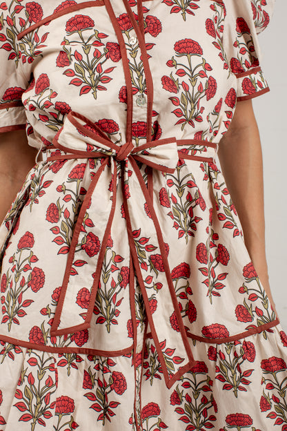 Close-up of a cream-colored dress with a red and green floral block print, featuring a matching fabric tie belt at the waist.