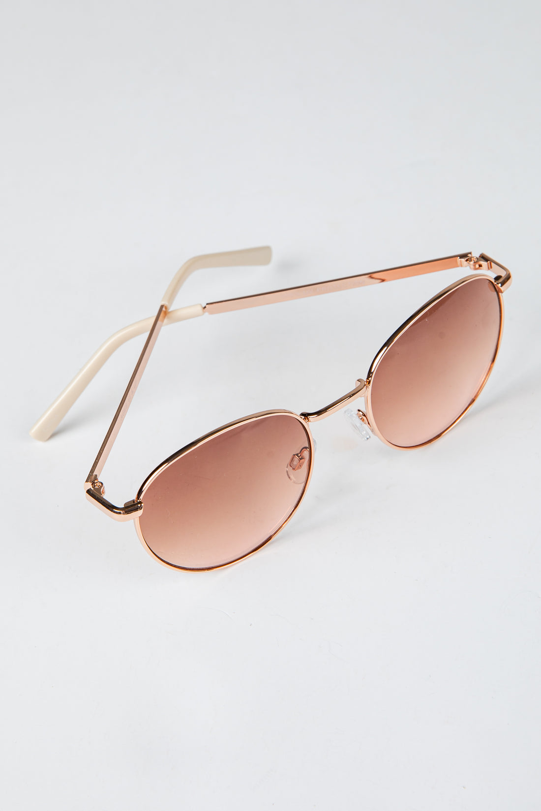 Rose gold sunglasses with rose gold lenses on a light gray background