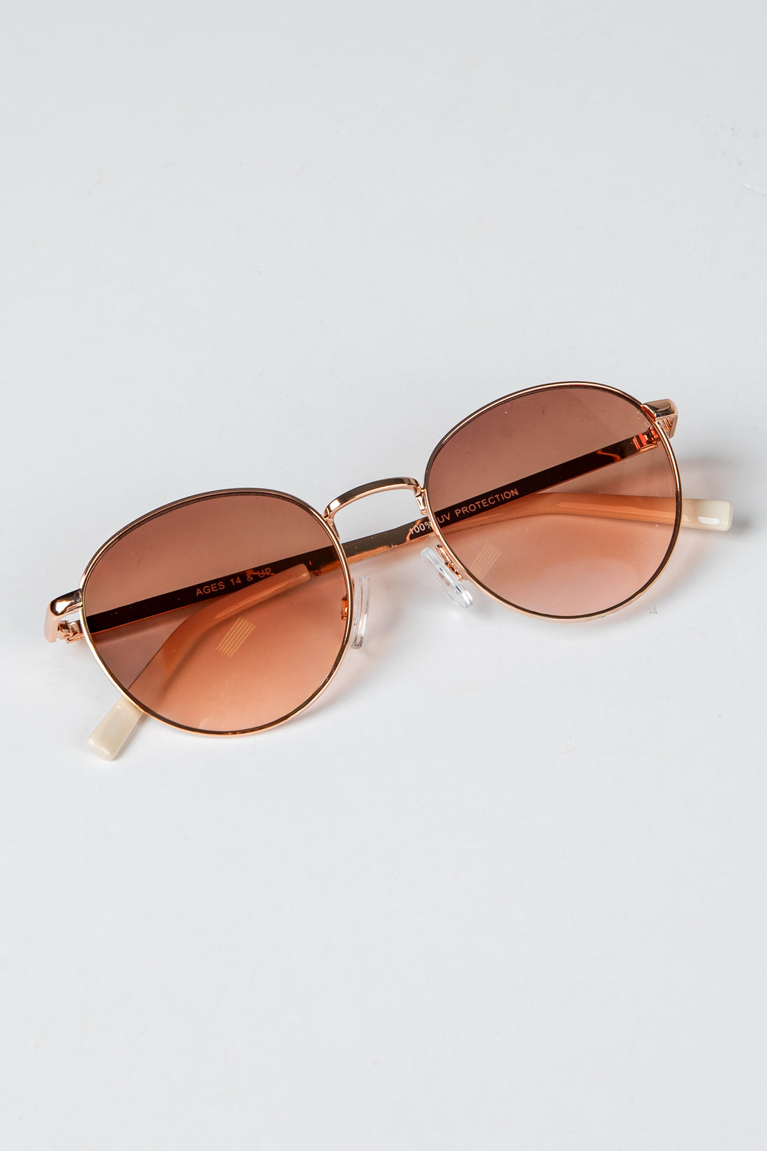 Sunglasses with rose gold frame and brown lenses on a light gray background