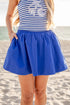 Person wearing a blue and white striped top with shell designs and a blue skirt on a beach.