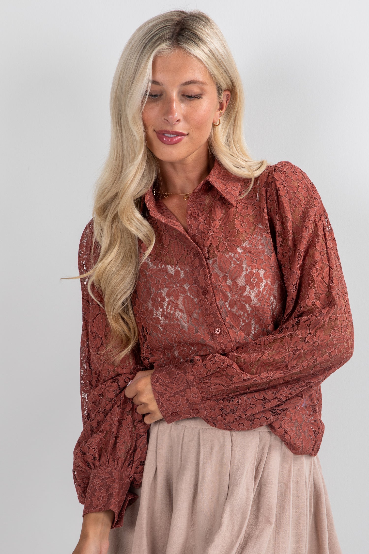 Woman wearing a rust-colored lace blouse against a white background