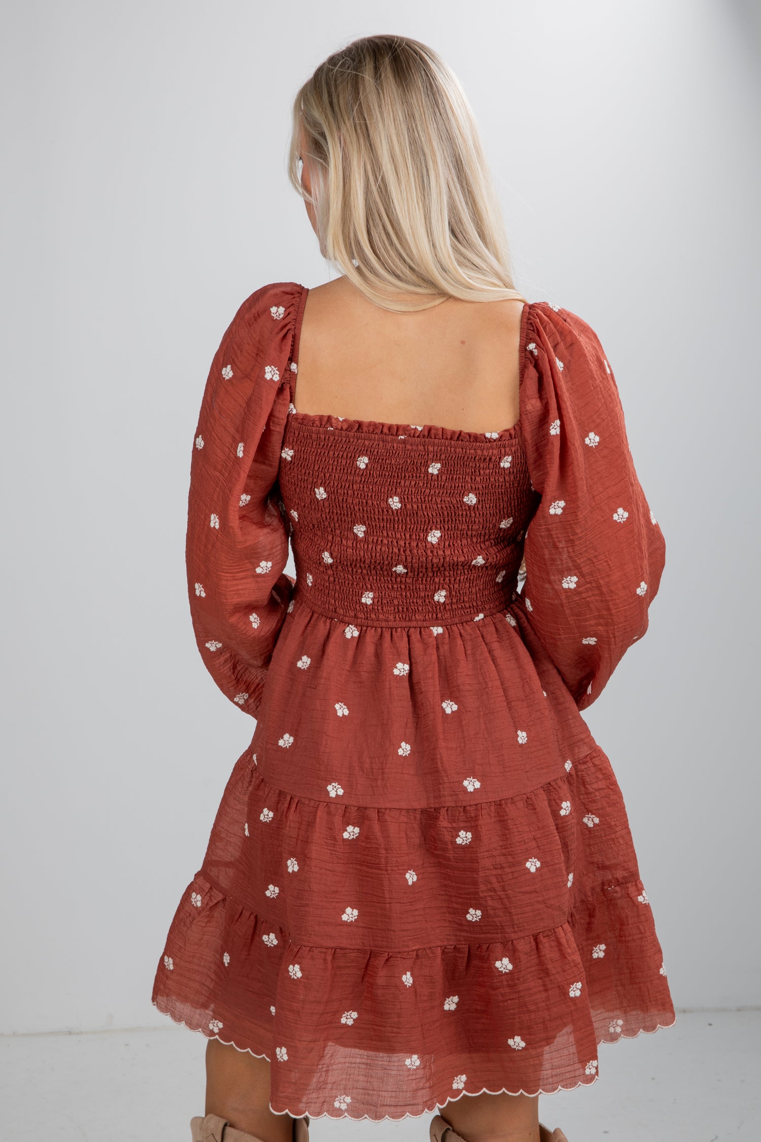 Woman wearing a rust-colored dress with floral pattern on a white background