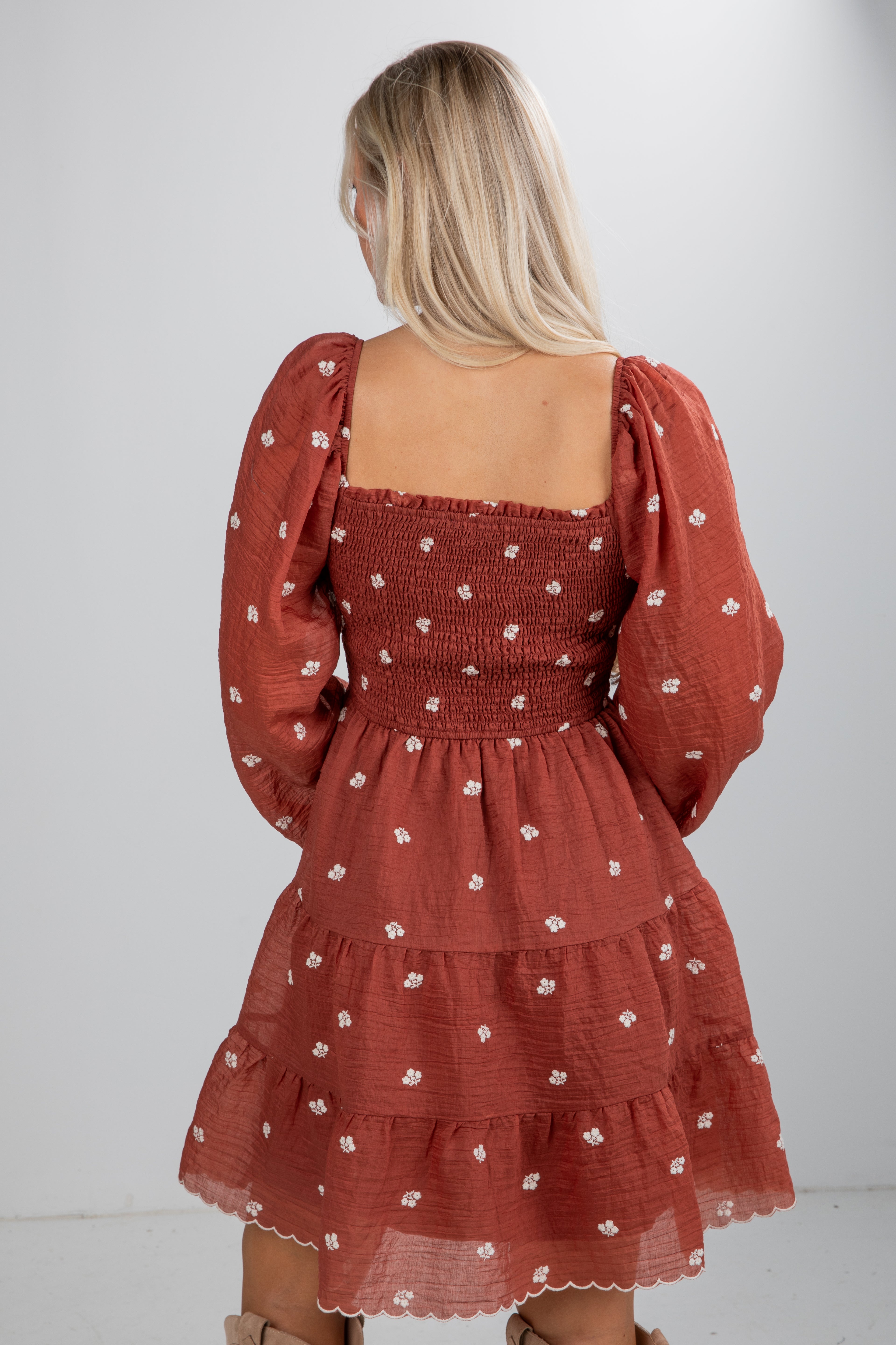 Woman wearing a rust-colored dress with floral pattern on a white background