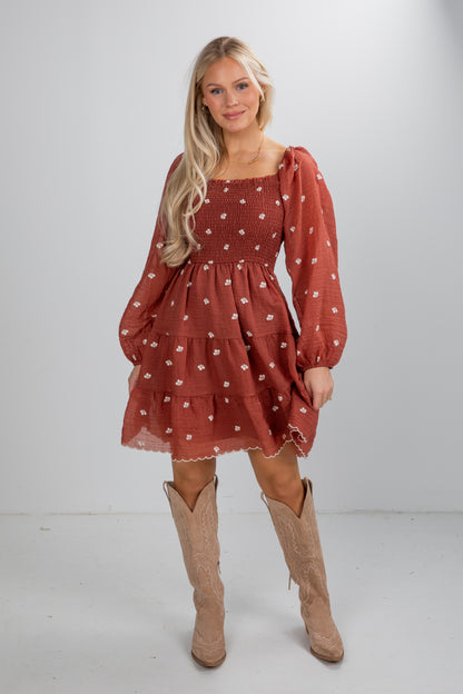 Woman wearing a red patterned dress with long sleeves and beige boots on a white background