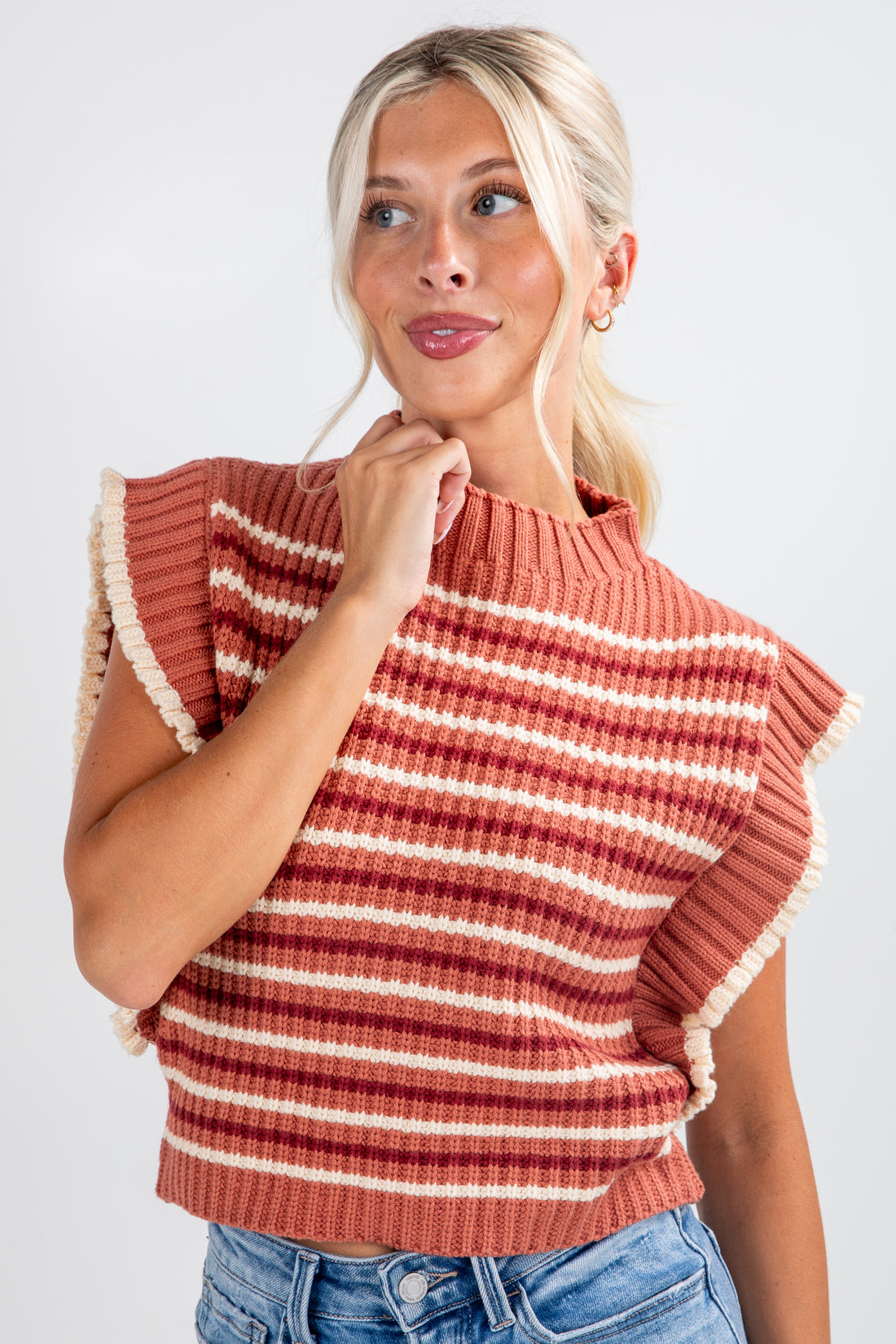 Woman wearing a rust-colored striped sweater with ruffled shoulders against a white background