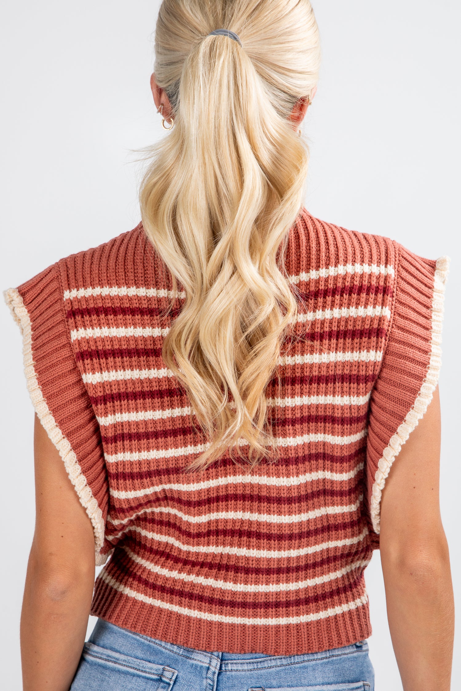 Person wearing a striped sleeveless sweater with ruffled edges on a plain background