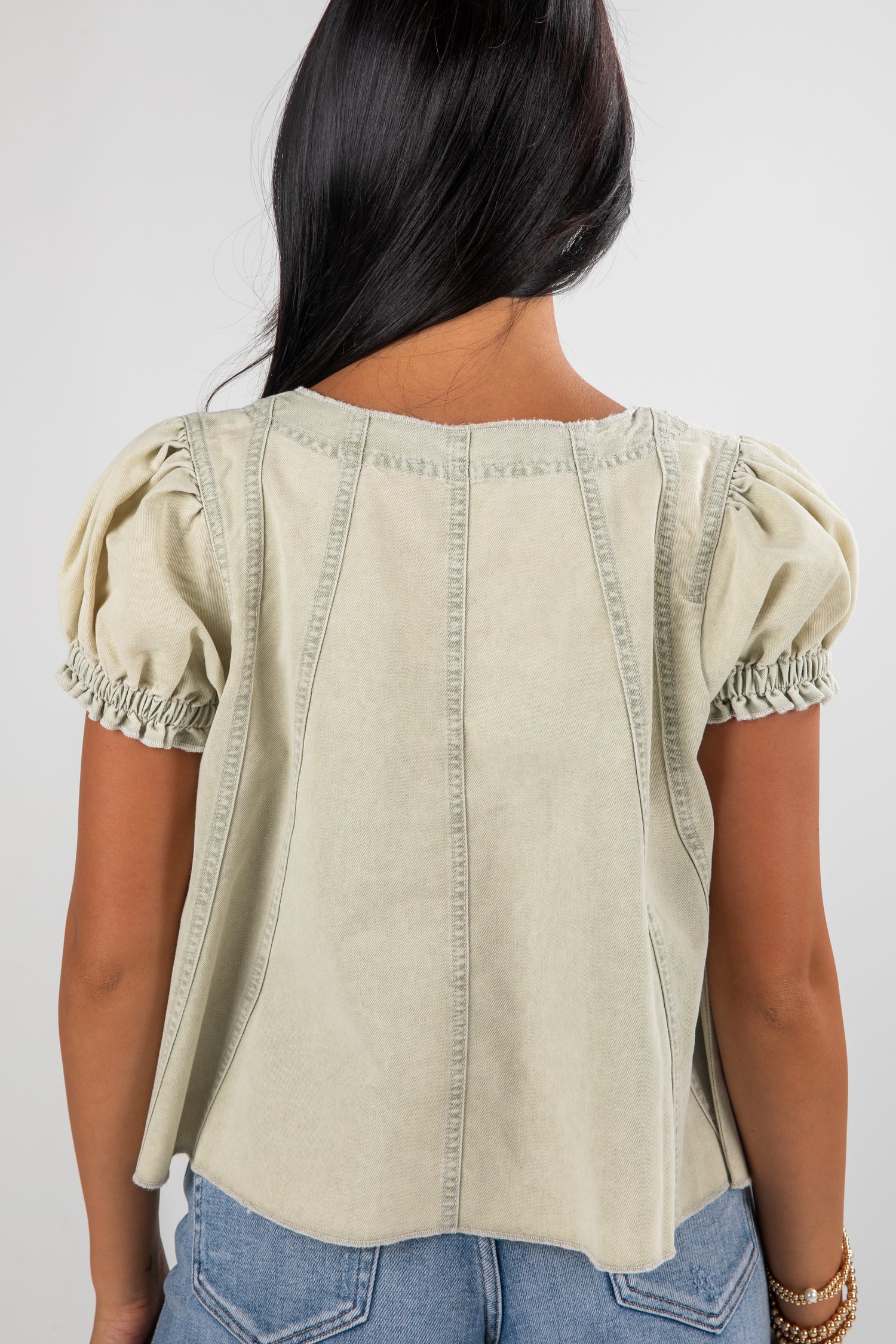 Woman wearing a beige top with puffed sleeves on a plain background