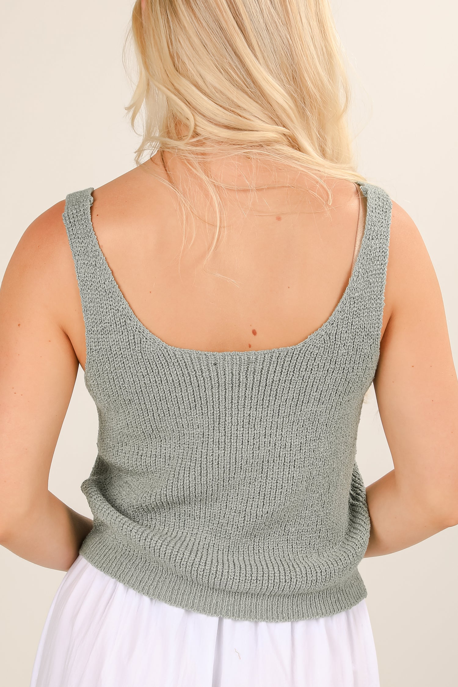 Person wearing a green knitted tank top against a neutral background