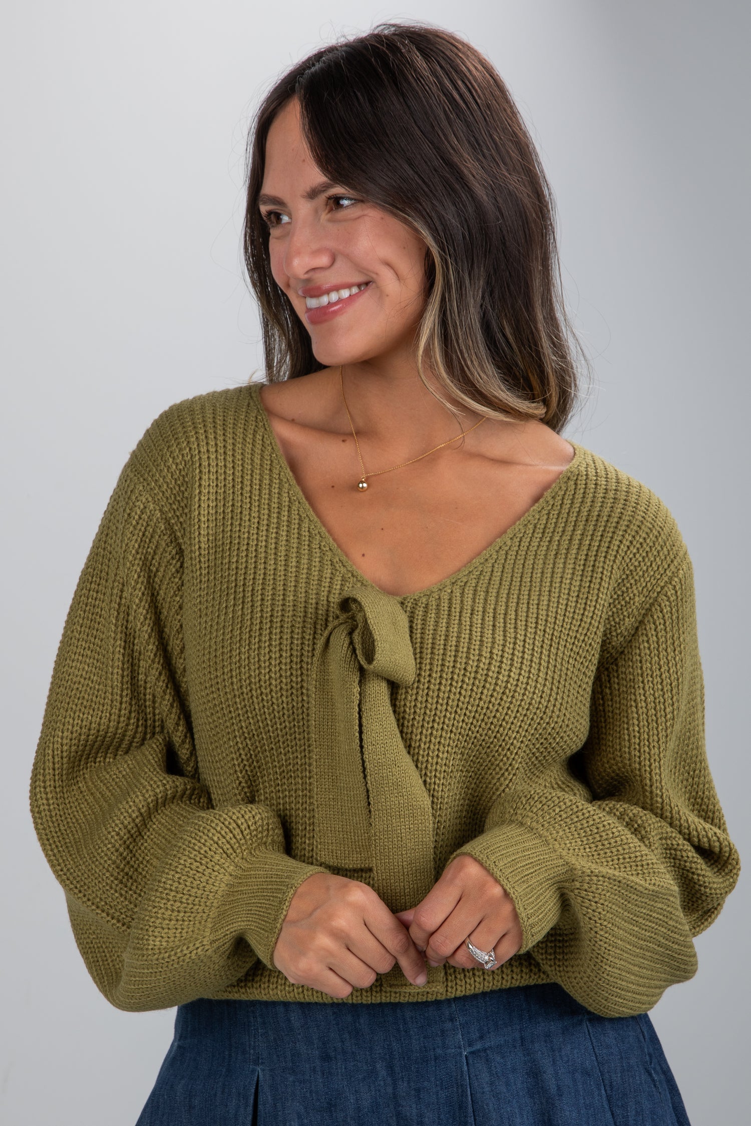 Woman wearing a green knitted sweater with a tie detail on a gray background