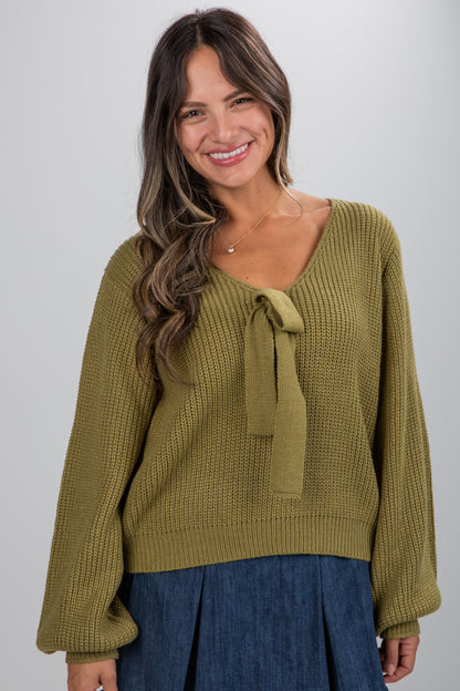 Woman wearing a green sweater with a tie detail on a gray background