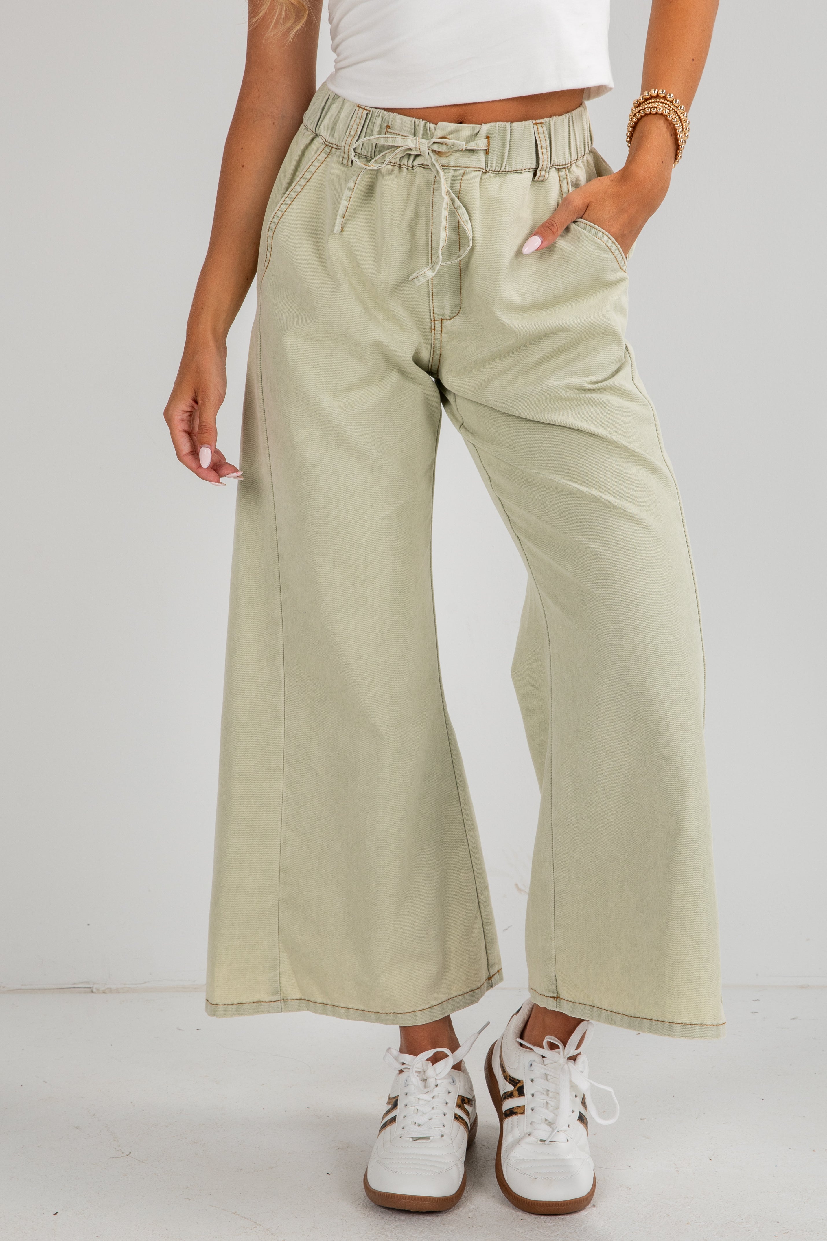 Person wearing light green wide-leg pants with a white background