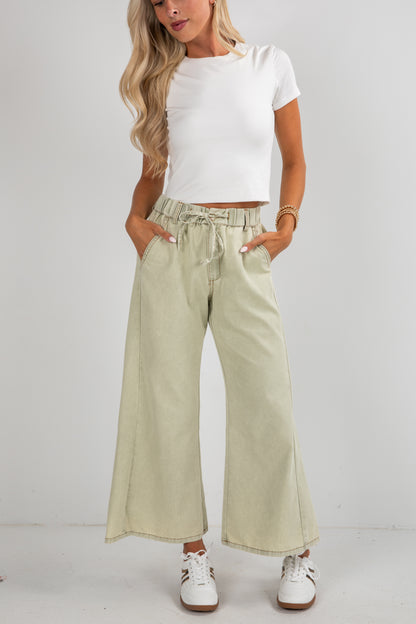 Woman wearing light-colored wide-leg pants and a white top on a plain background