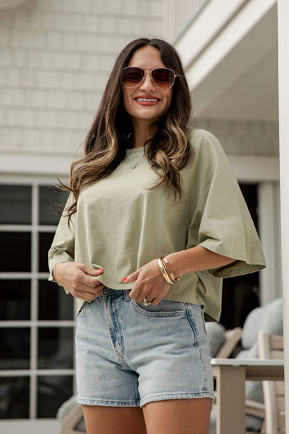 Woman wearing a light green top and denim shorts outdoors.