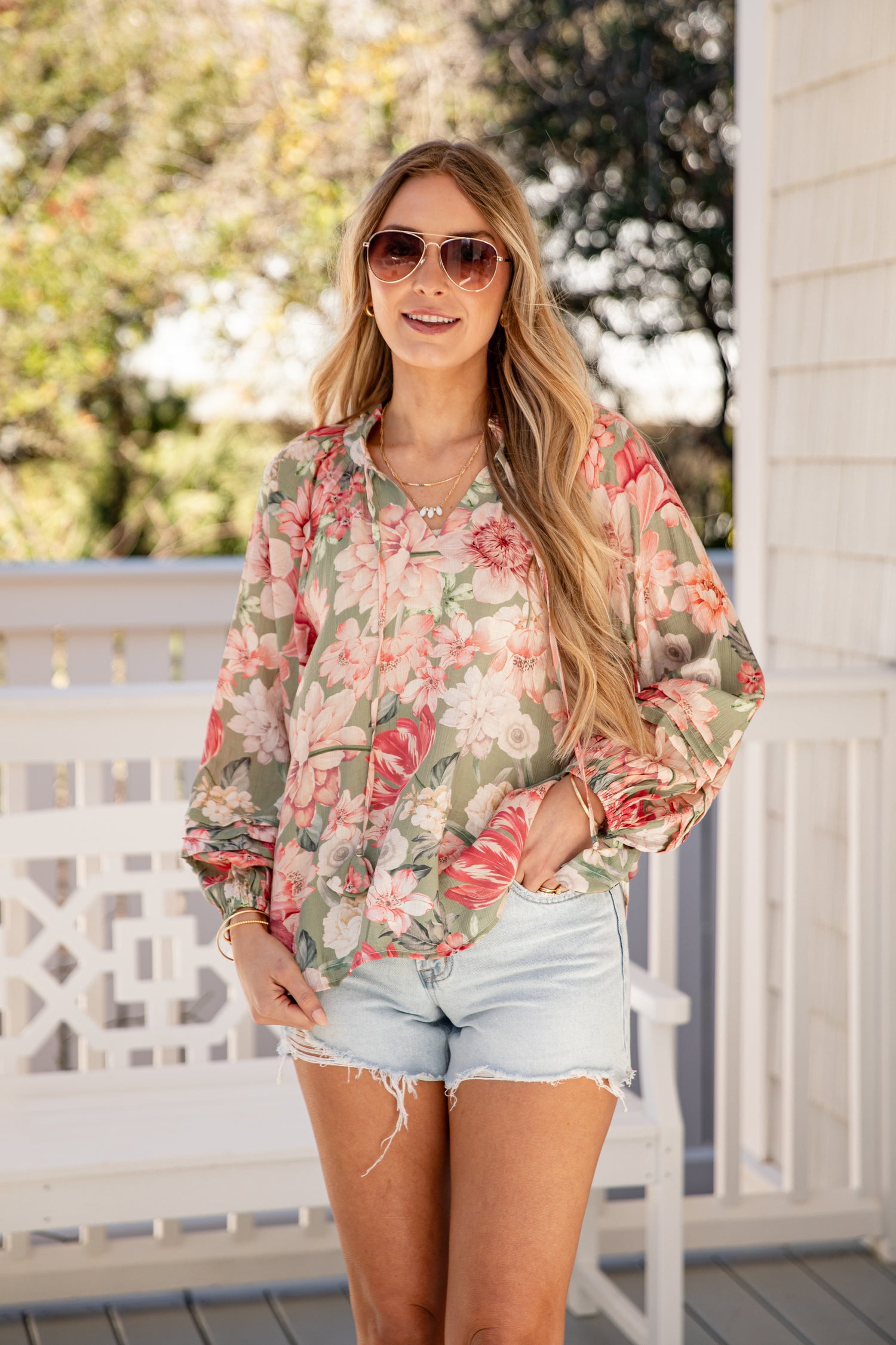 Woman wearing a floral blouse and denim shorts on a porch.