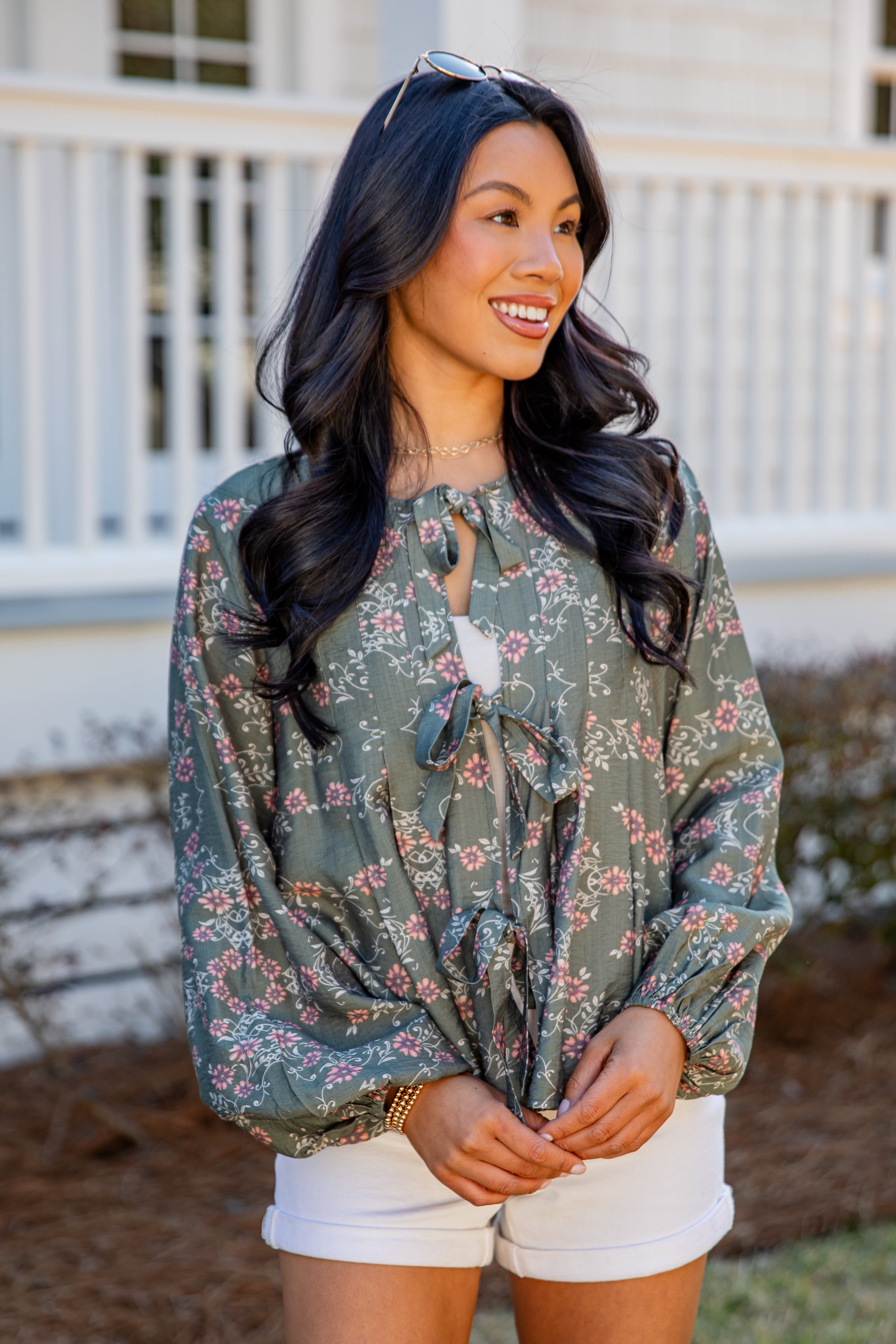 Woman wearing a floral blouse and white shorts standing in front of a white railing.