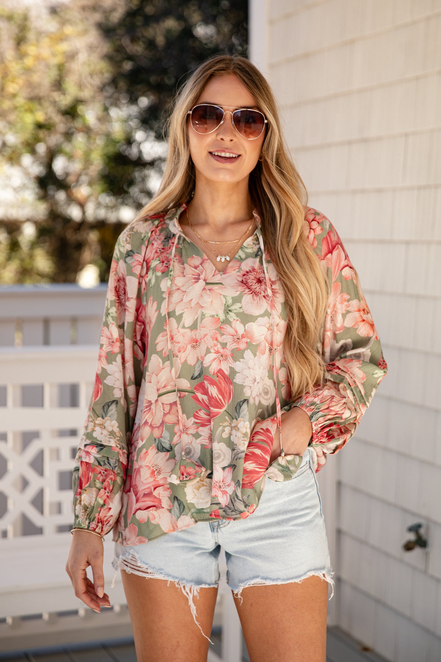 Woman wearing a floral blouse and denim shorts outdoors.