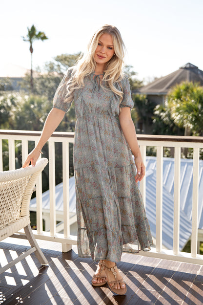 Woman in a patterned dress standing on a balcony with a scenic background