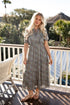 Woman in a patterned dress standing on a balcony with greenery in the background