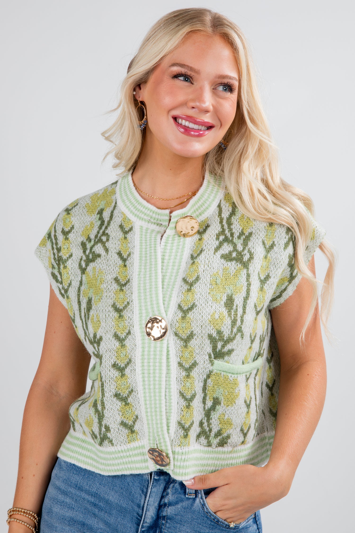 Woman wearing a green knitted vest with floral patterns on a plain background