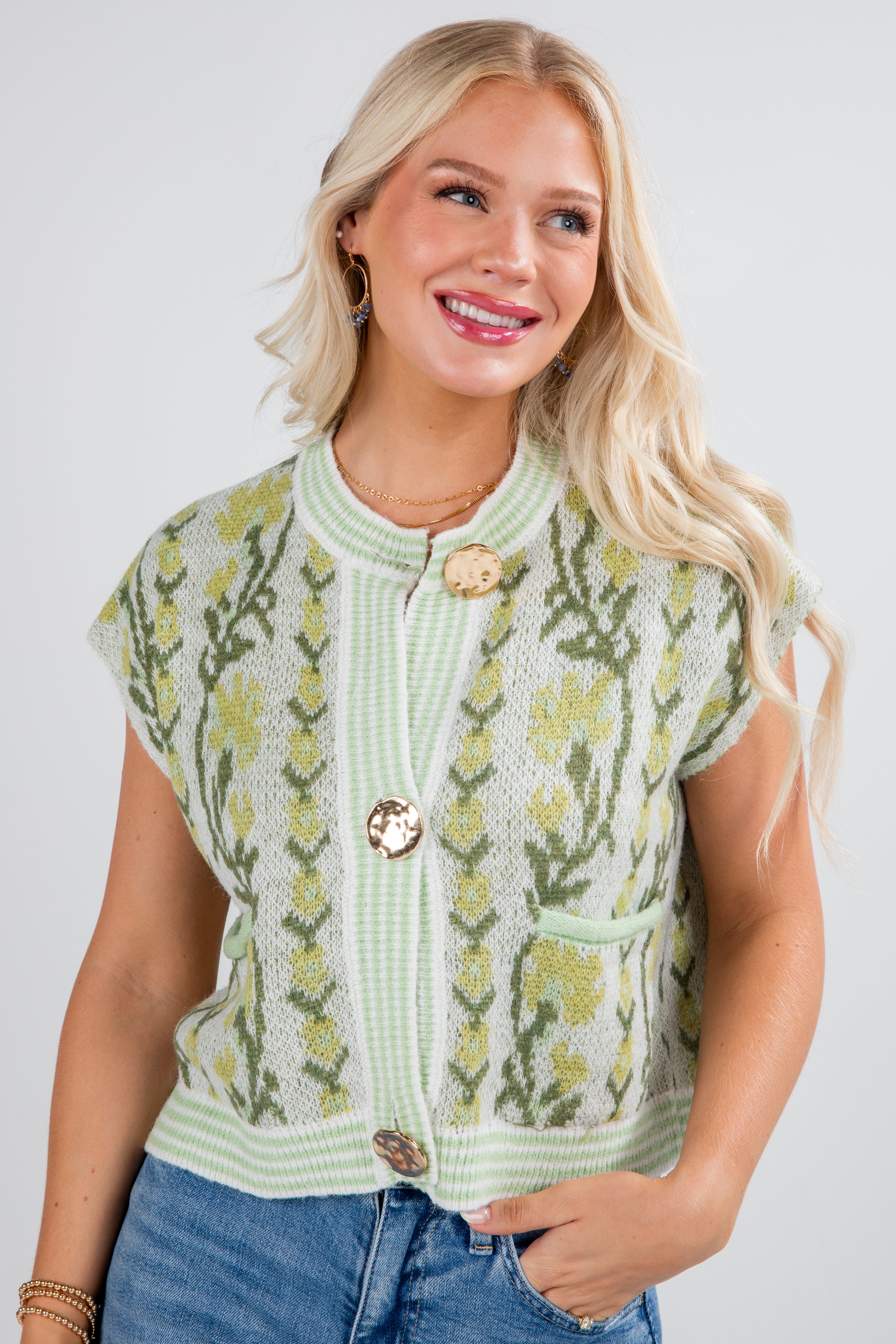 Woman wearing a green knitted vest with floral patterns on a plain background