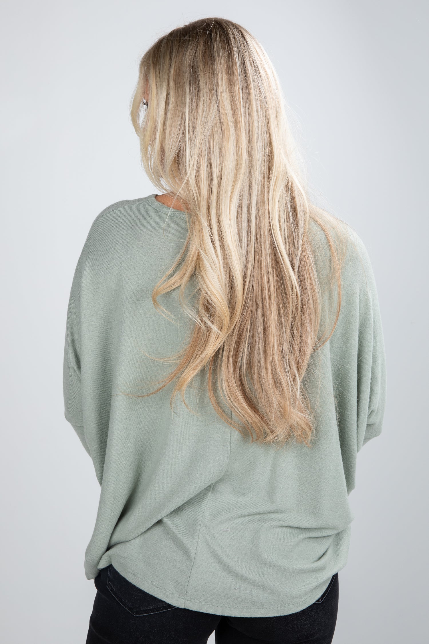 Person wearing a light green sweater with long blonde hair on a plain background