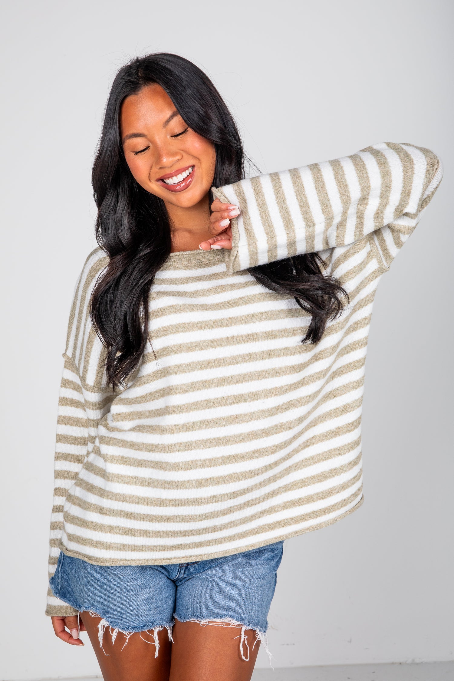 Woman wearing a striped sweater and denim shorts against a plain background