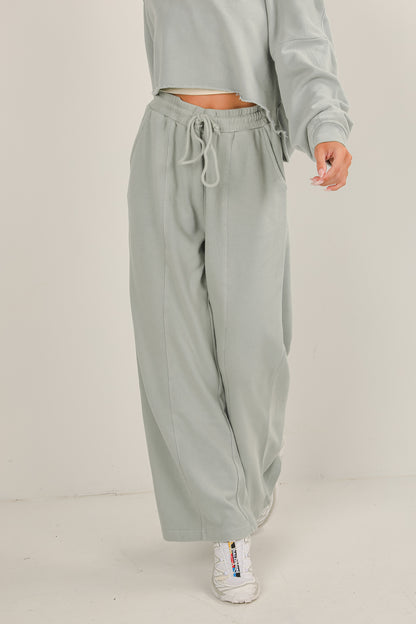 Person wearing light gray sweatpants and a matching top on a plain background