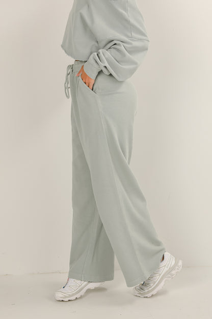 Person wearing a light gray outfit with wide-leg pants on a plain background