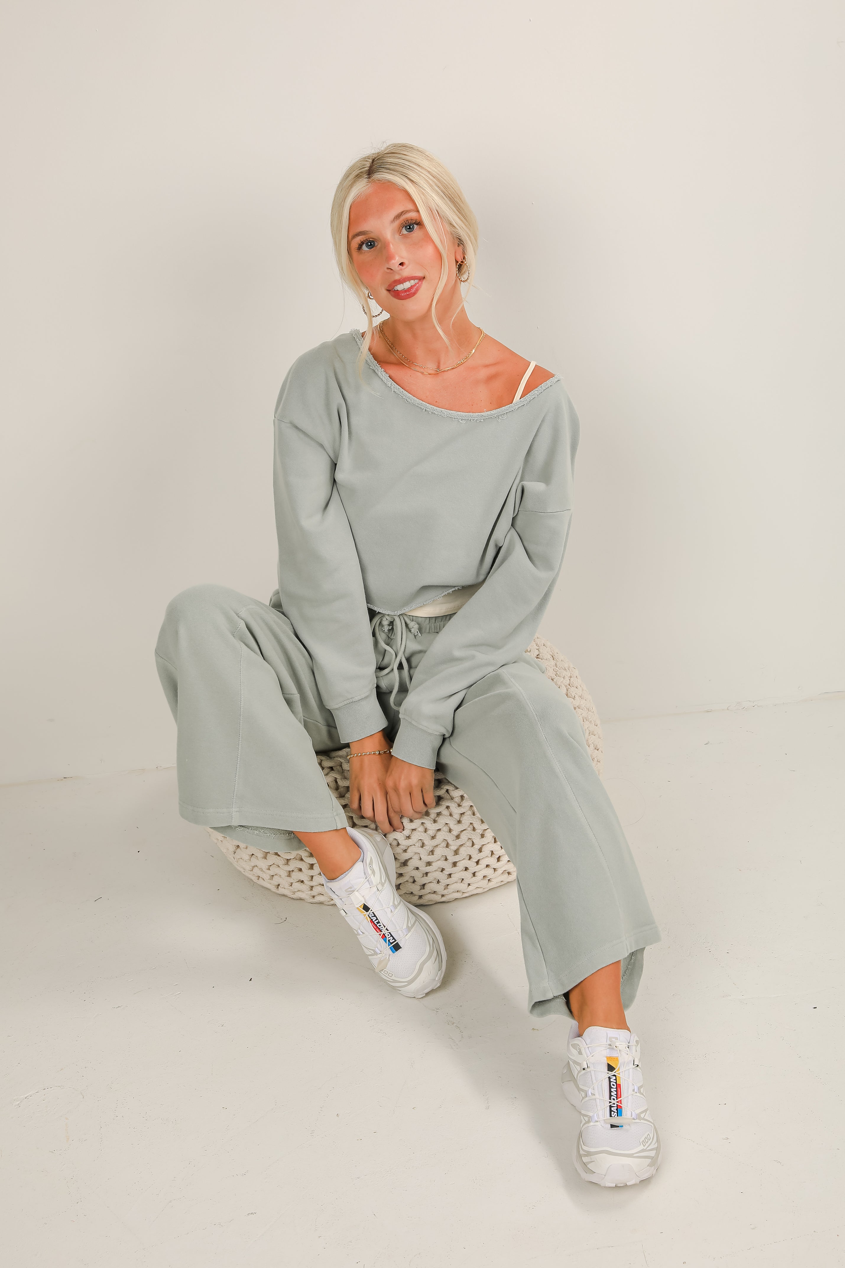 Woman wearing a light gray outfit sitting on a white floor.
