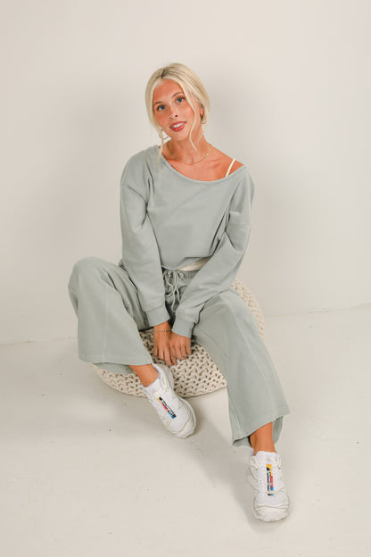 Woman wearing a light gray outfit sitting on a white floor.