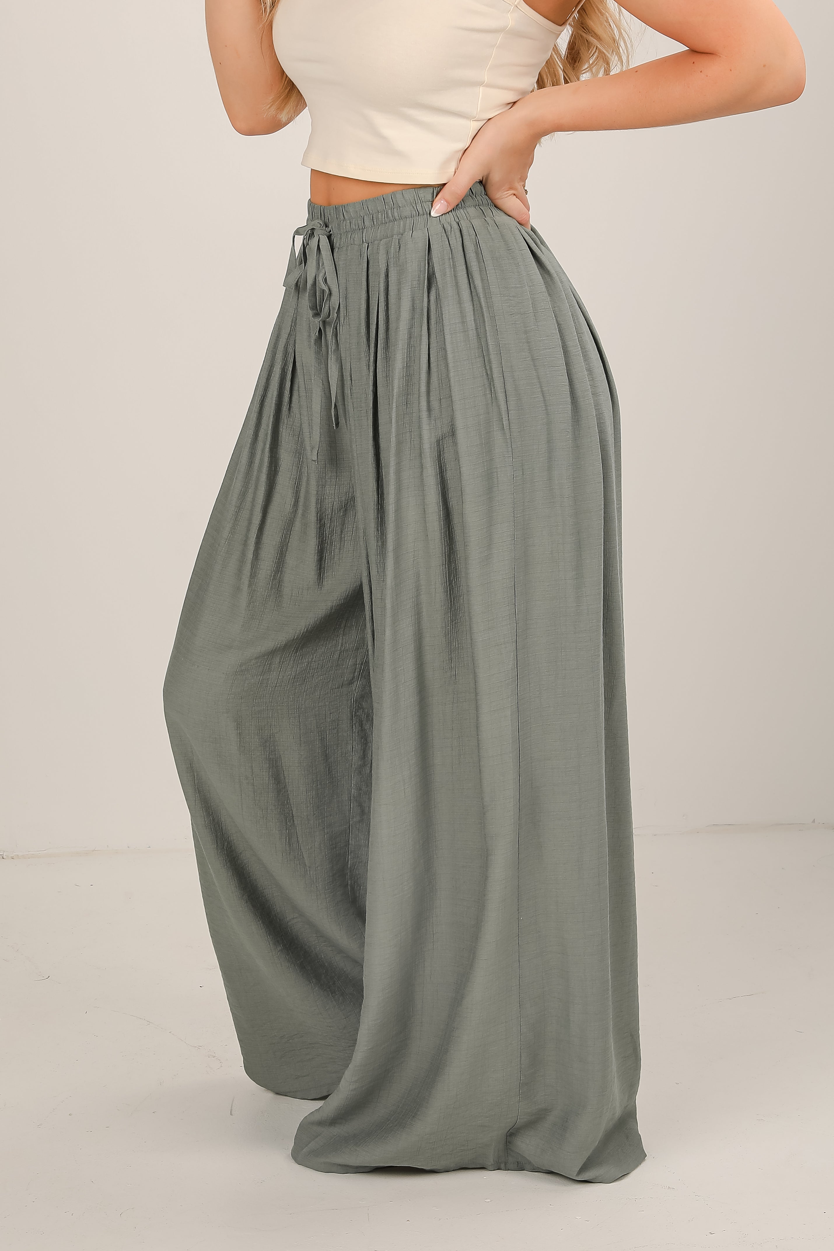 Person wearing a beige top and green wide-leg pants on a plain background