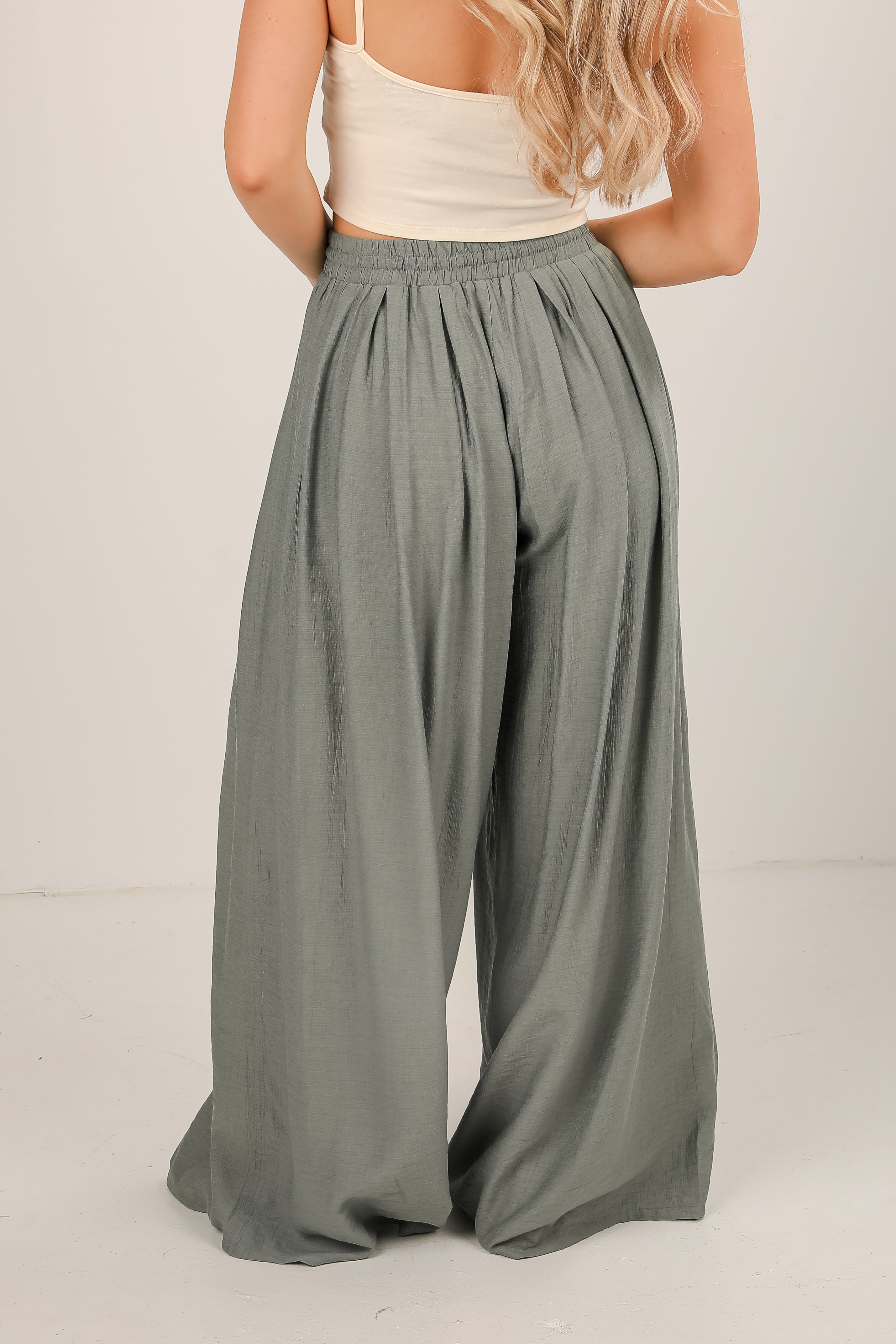 Person wearing light green wide-leg pants and a white top on a plain background