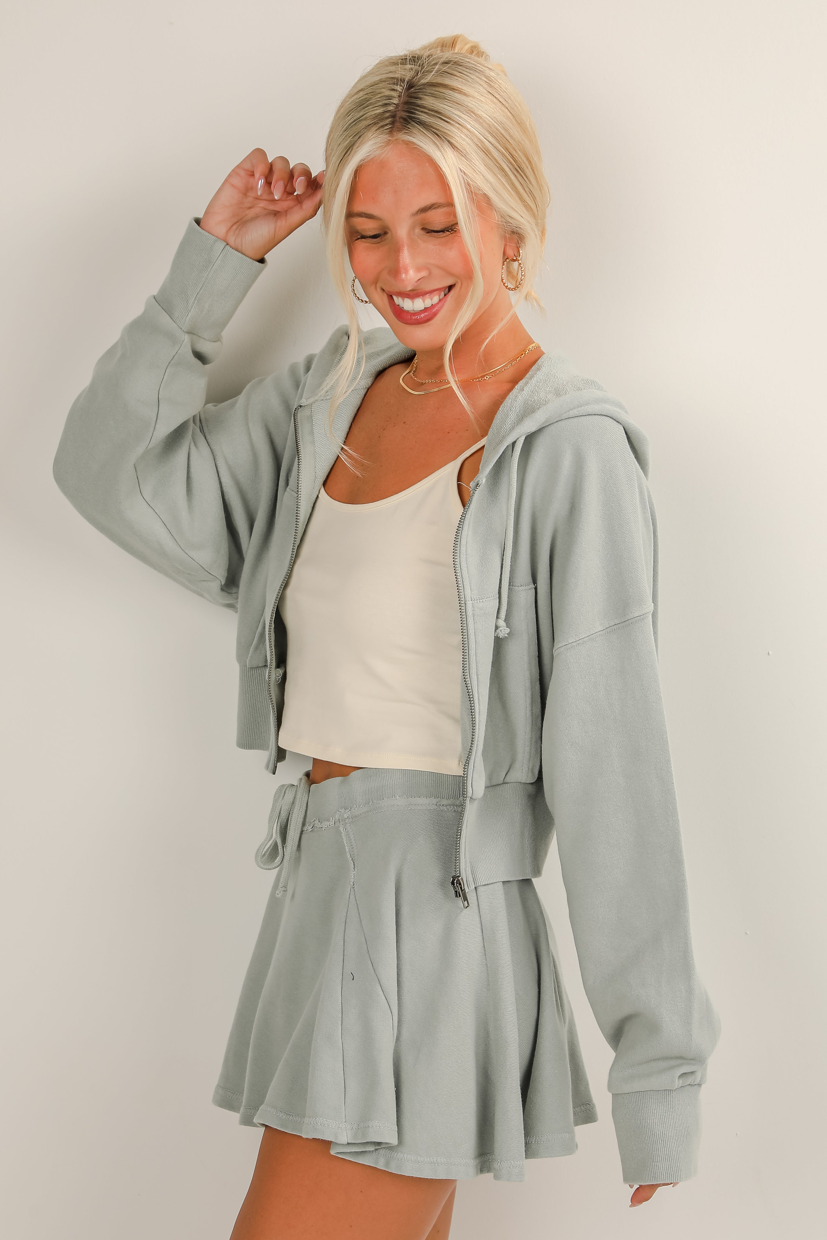 Woman wearing a light gray hoodie and shorts set on a plain background