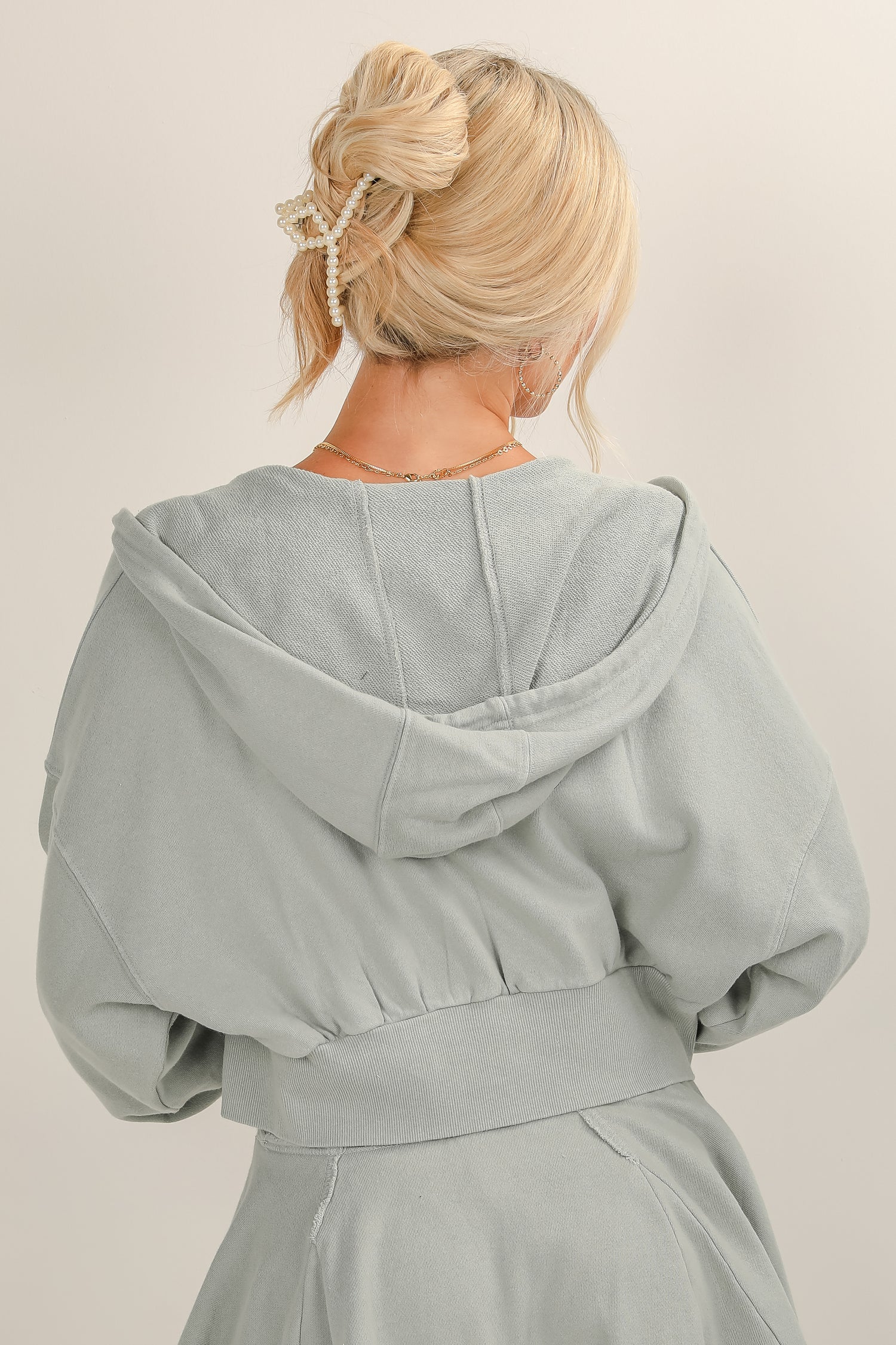 Person wearing a light gray hooded garment against a plain background